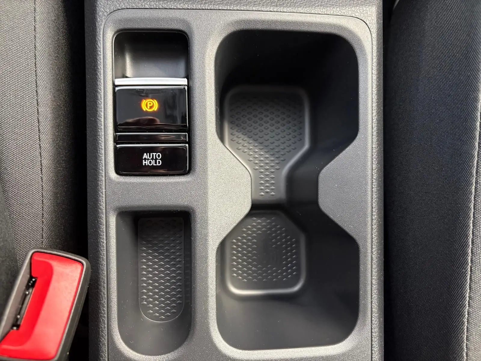 Gros plan sur la console centrale du Volkswagen Caddy 2025, avec bouton frein à main électronique et porte-gobelets noirs.