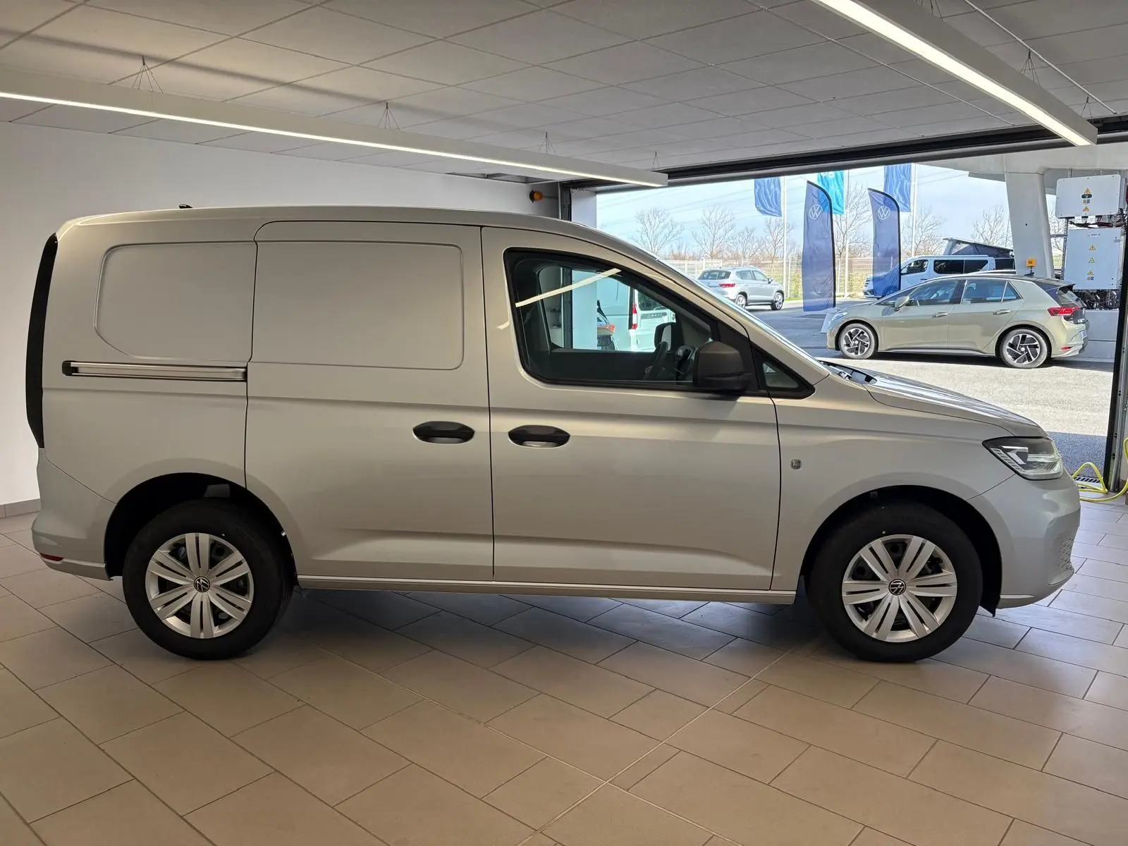 Volkswagen Caddy 2025 gris argent vu de profil côté gauche dans un showroom lumineux.