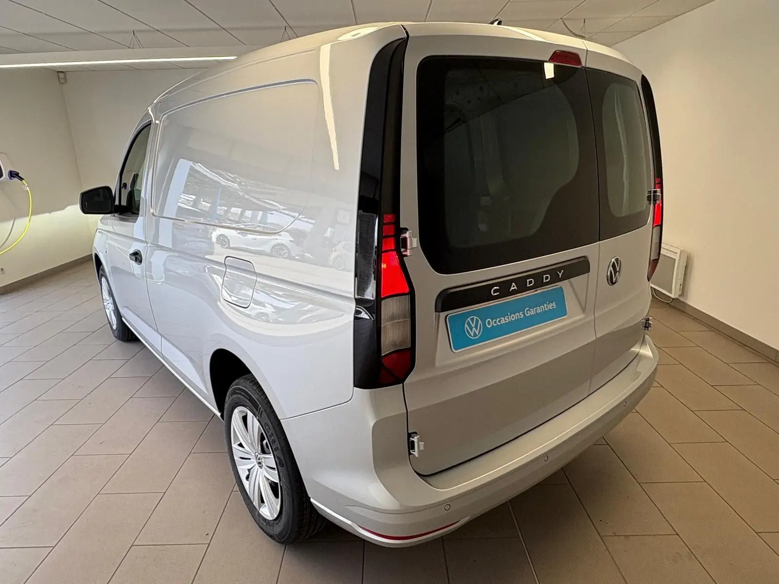Vue 3/4 arrière droite du Volkswagen Caddy gris argent 2025, fourgon utilitaire avec portes arrière vitrées et feux verticaux.
