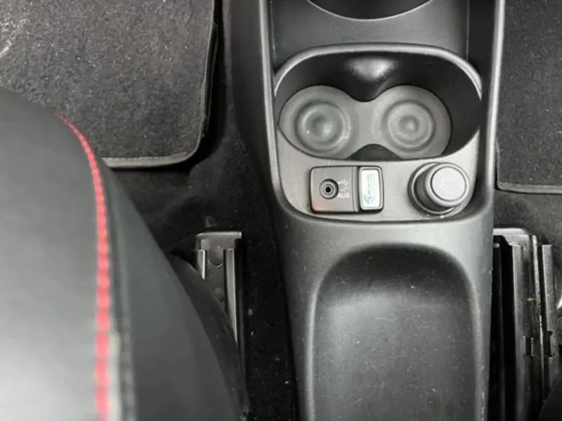 Vue plongeante sur la console centrale noire de l'Abarth 500 2013 avec prises auxiliaire et USB et porte-gobelets.