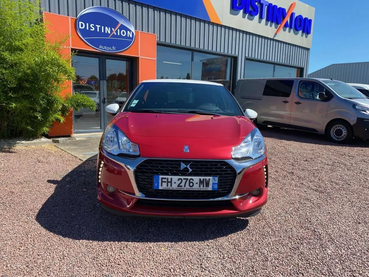 Vue de face d'une DS3 rouge au toit blanc, stationnée devant un bâtiment avec enseigne Distinxion.