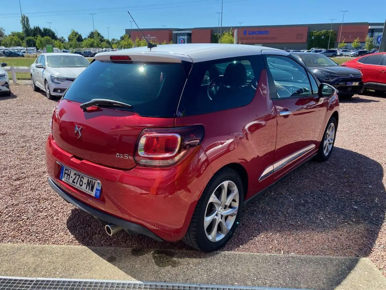 Vue 3/4 arrière droite d'une DS3 rouge à toit blanc, avec jantes alliage et feu arrière carré distinctif.