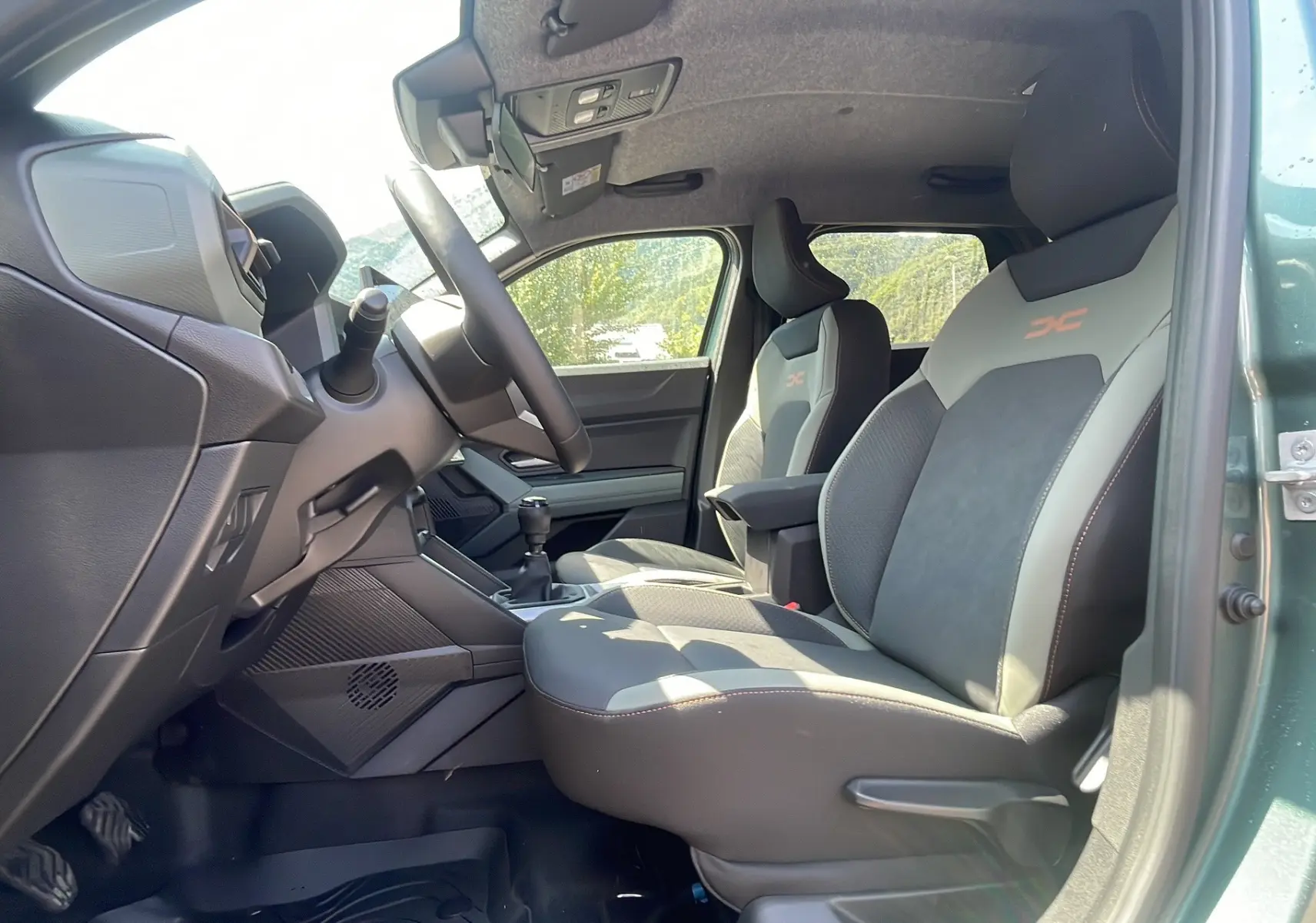 Vue intérieure côté conducteur du Dacia Duster 2025 vert cèdre, sièges sport avec logo orange et boîte manuelle visible.