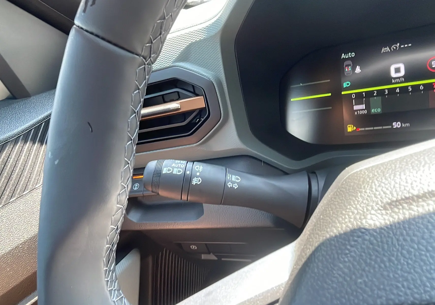 Gros plan sur le tableau de bord du Dacia Duster 2025, affichage numérique et commande des phares visibles.