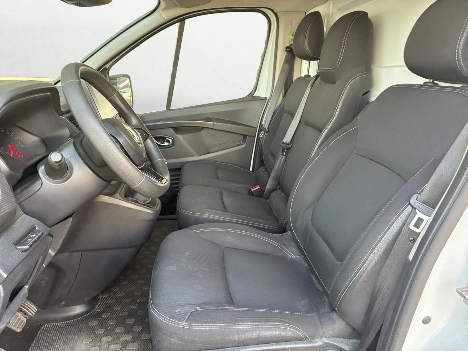 Vue intérieure côté conducteur du Renault Trafic Fourgon blanc 2022, sièges noirs avec surpiqûres grises et volant multifonction.