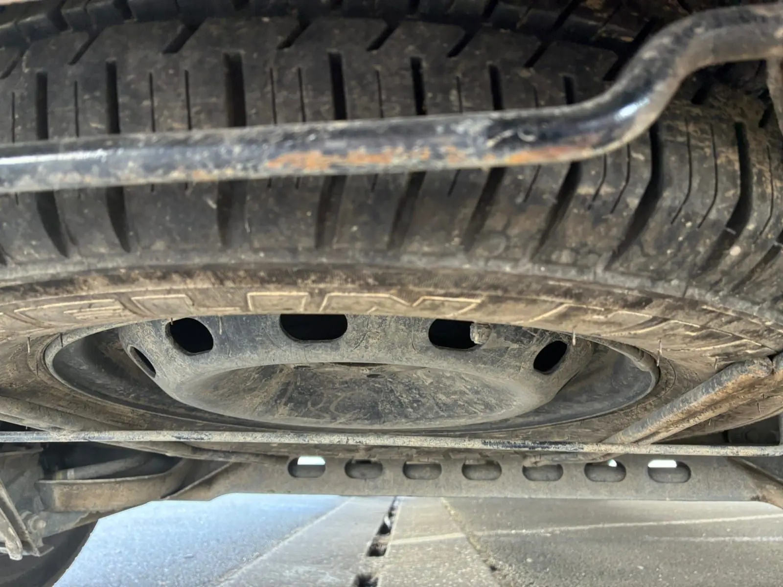 Vue en contre-plongée du pneu de secours sous un Renault Trafic Fourgon blanc, montrant la roue de secours et le châssis inférieur.