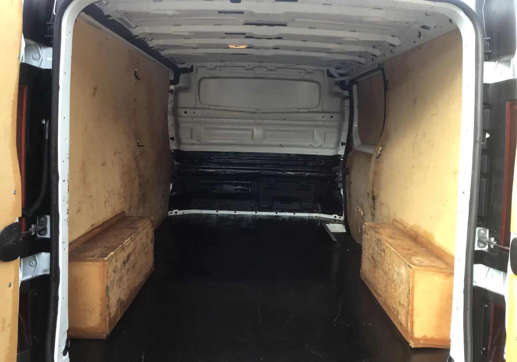 Intérieur du fourgon Renault Trafic blanc vu de l'arrière, avec parois en bois et plancher noir aménagé.