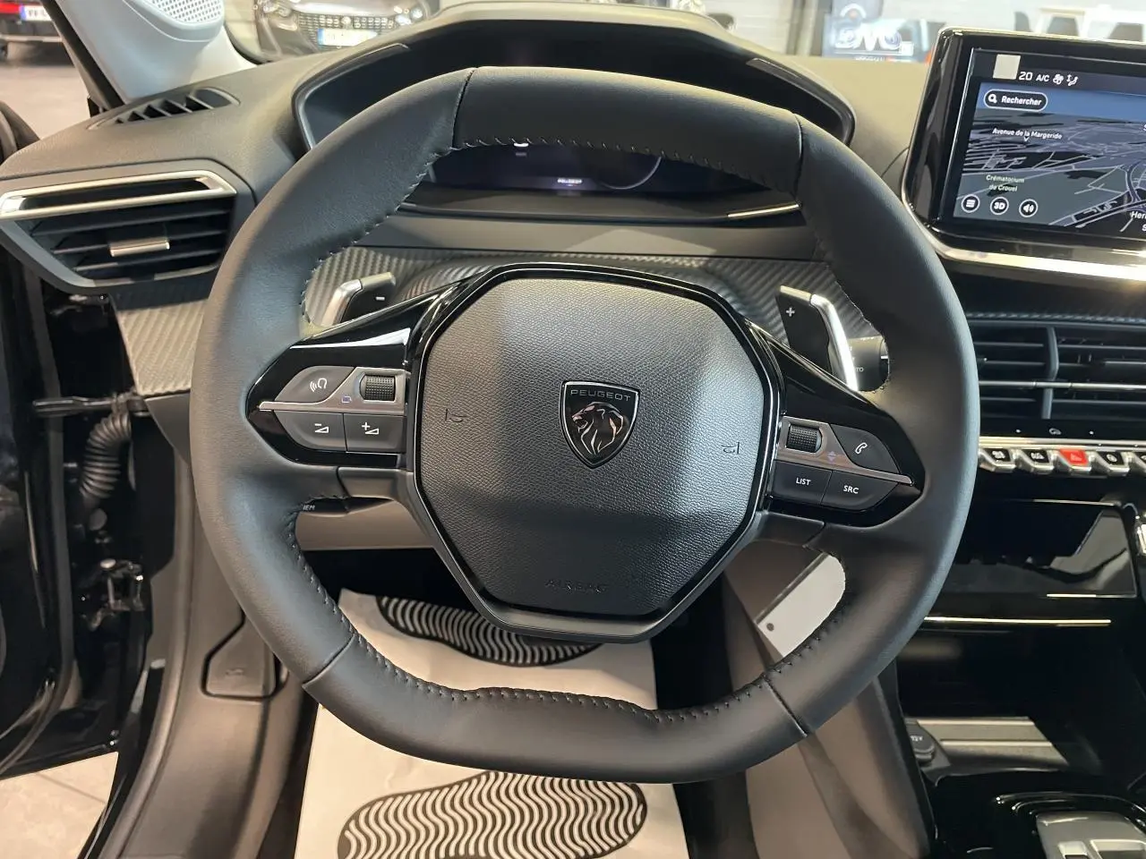 Vue rapprochée du volant cuir noir et du tableau de bord numérique de la Peugeot 208 hybride 2025 Allure.