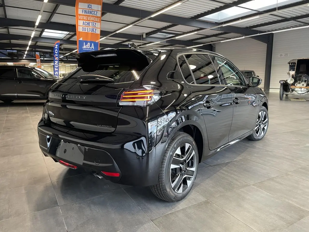 Vue 3/4 arrière droite d'une Peugeot 208 noire hybride 2025 avec jantes alliage 16 pouces et feux LED distinctifs.