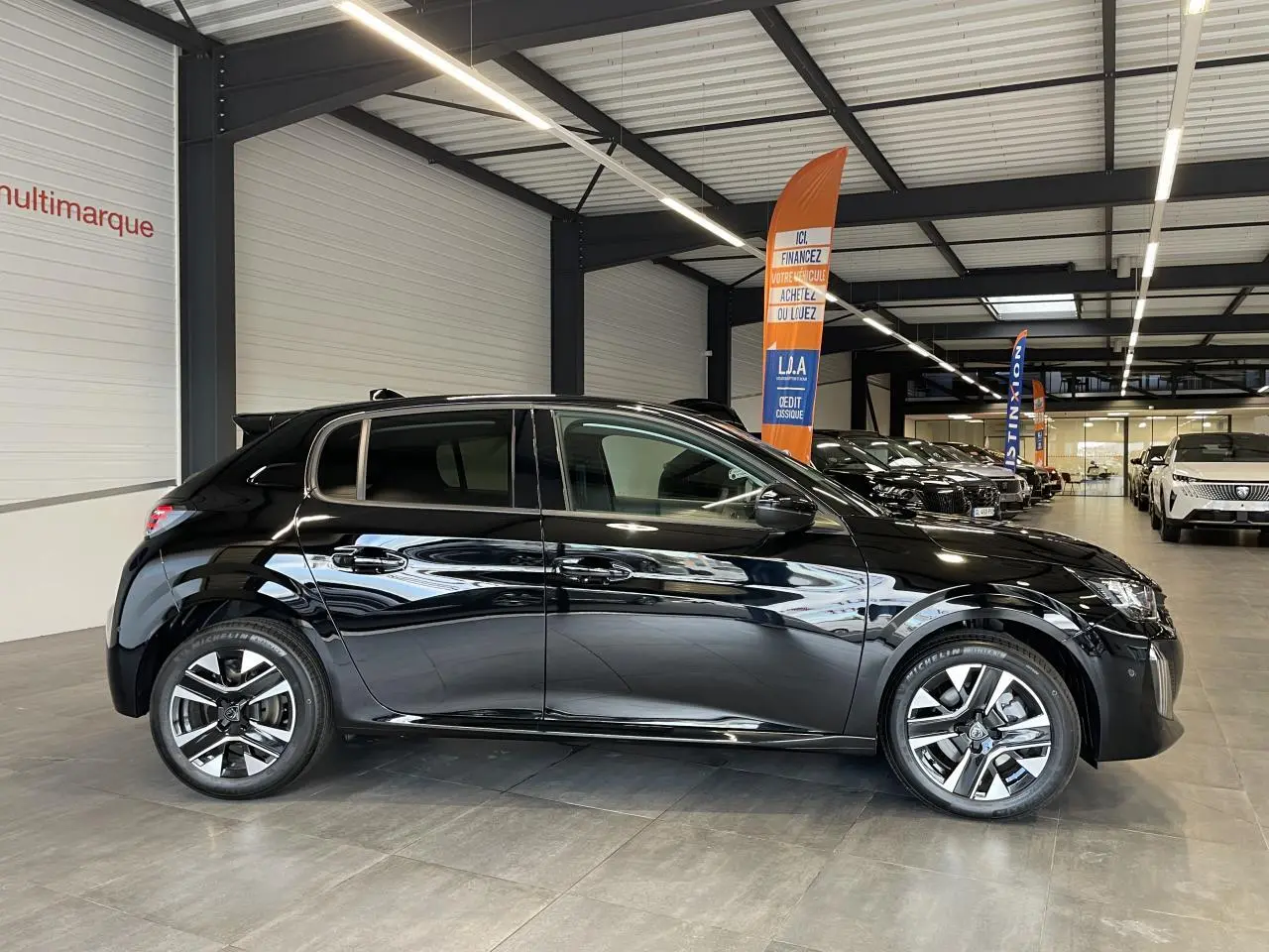 Peugeot 208 noire vue de profil côté gauche en intérieur, avec jantes alliage bi-tons et vitres teintées.