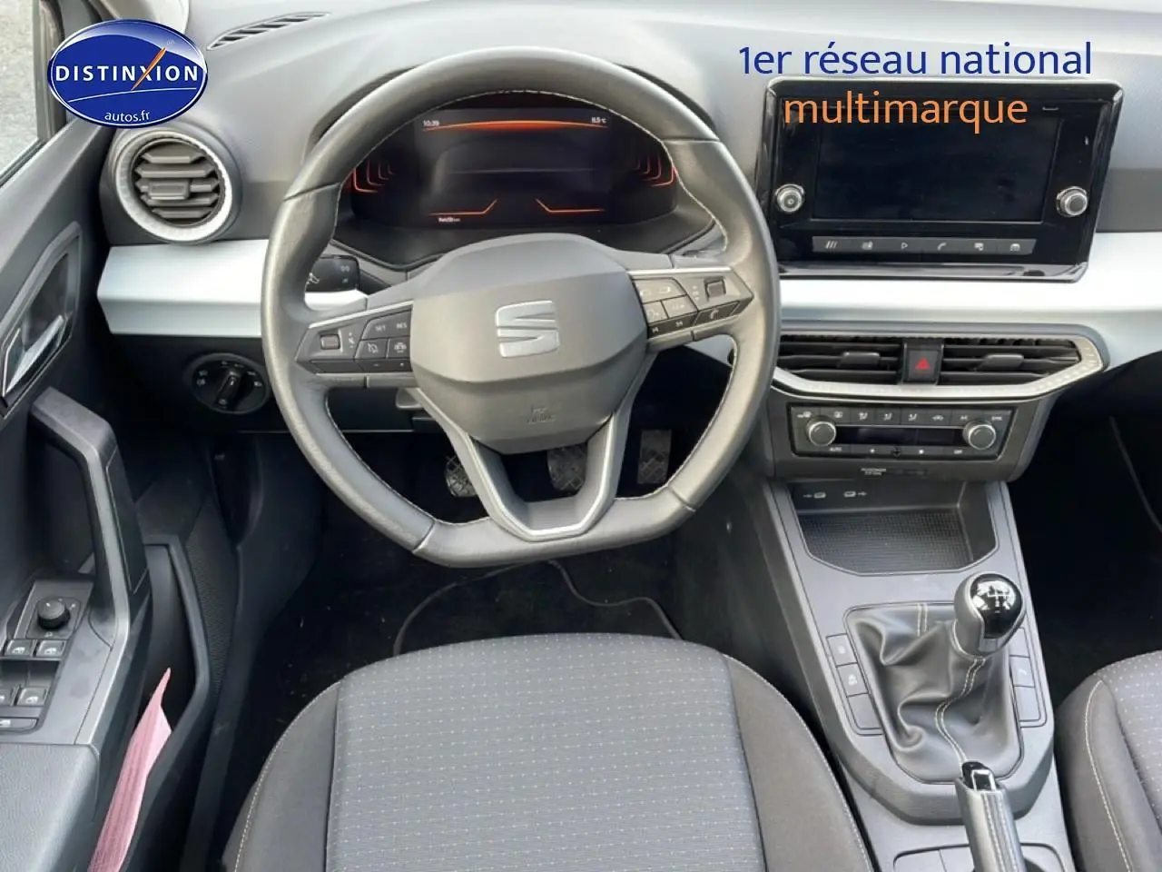 Vue intérieure frontale du poste de conduite de la SEAT Ibiza blanc Nevada 2025 avec volant sport et boîte manuelle.