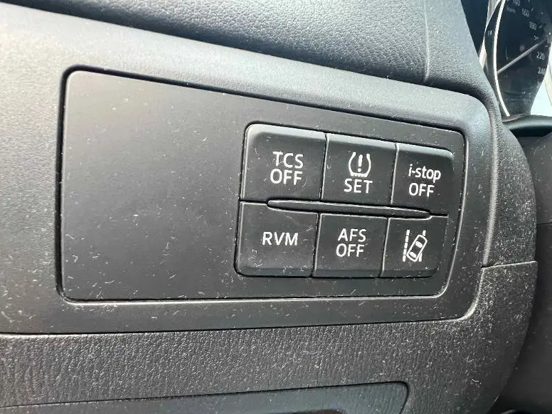 Gros plan sur les boutons de commande noirs du tableau de bord du Mazda CX-5 2013, avec fonctions d'assistance visibles.