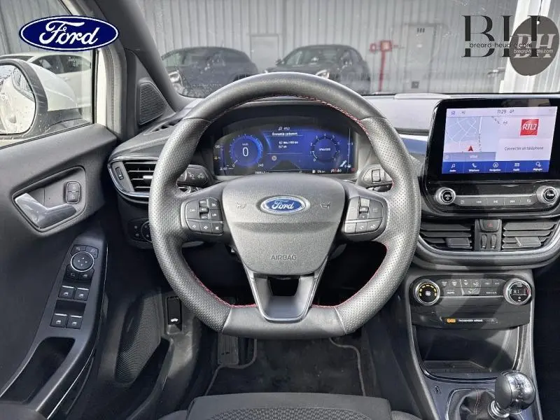 Vue intérieure centrée sur le volant cuir sport et le tableau de bord numérique du Ford Puma blanc, avec écran tactile et commandes au volant.