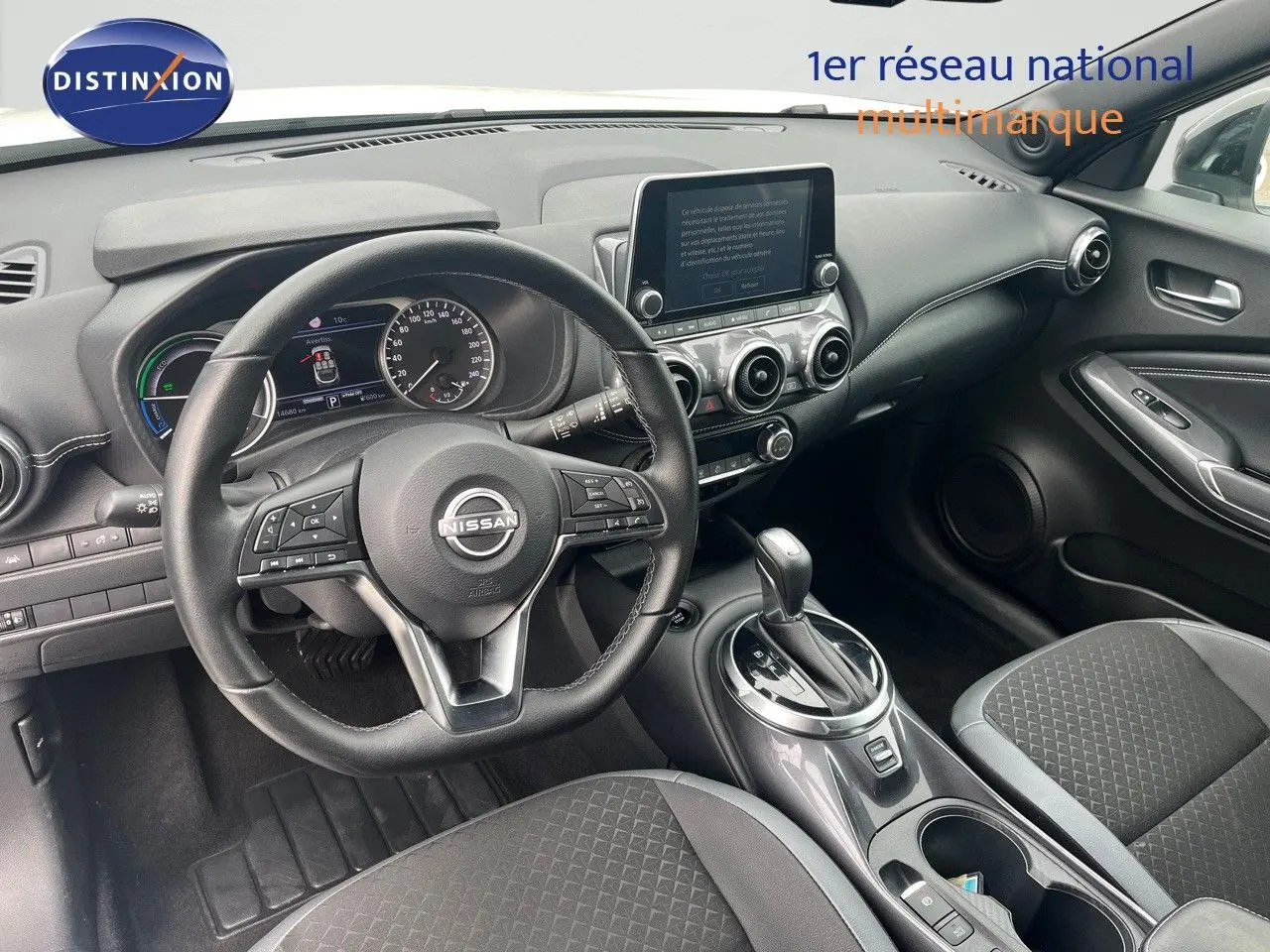 Vue intérieure côté conducteur du Nissan Juke 2024, montrant le volant, tableau de bord et console centrale en noir.