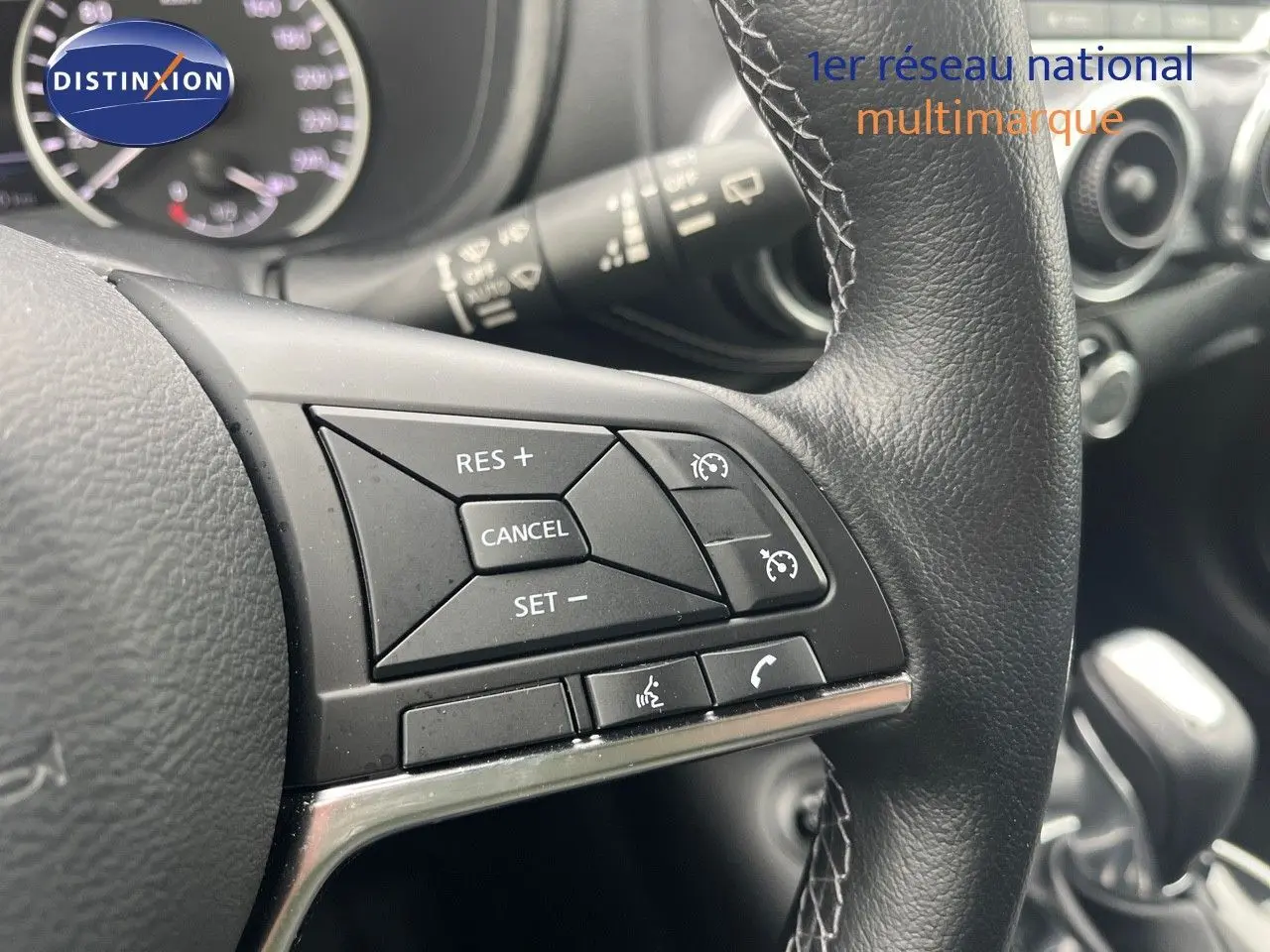 Gros plan sur les commandes au volant en cuir noir du Nissan Juke 2024, avec tableau de bord et levier de vitesses visibles en arrière-plan.