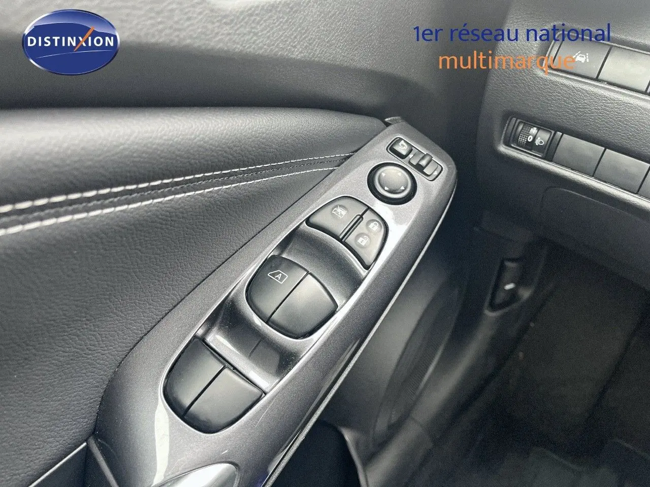 Vue rapprochée des commandes de lève-vitres côté conducteur sur la porte intérieure noire du Nissan Juke blanc nacré 2024.