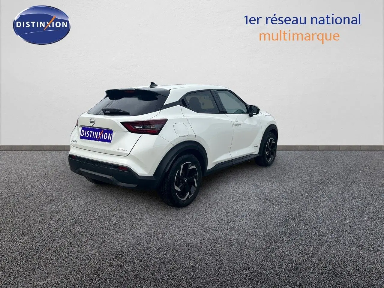 Nissan Juke blanc nacré 2024 en 3/4 arrière droit, SUV compact avec jantes noires et toit noir contrasté.