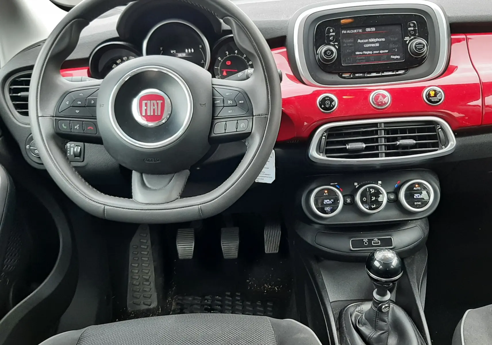 Vue intérieure avant de la Fiat 500X rouge de 2016, avec volant multifonction, tableau de bord rouge brillant et boîte manuelle.