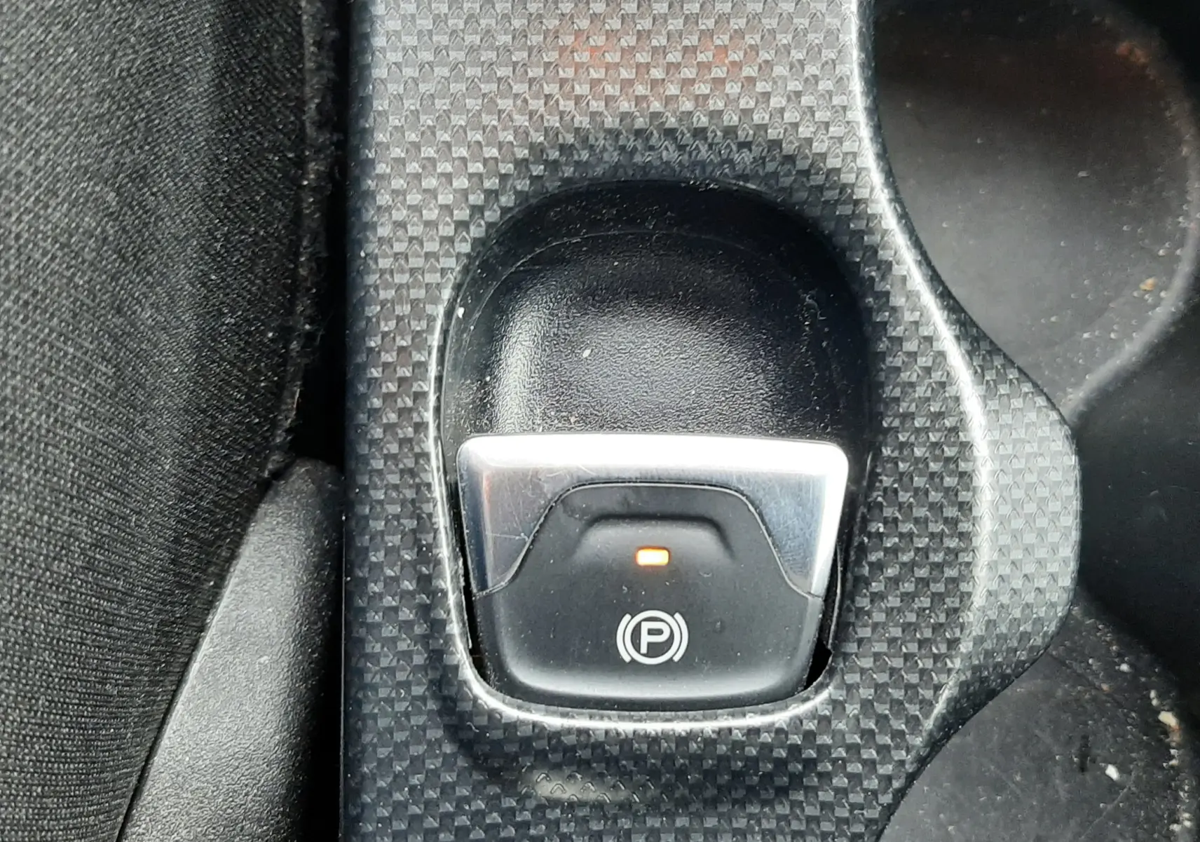 Gros plan sur le bouton de frein à main électrique allumé dans la console centrale d'une Fiat 500X rouge de 2016.