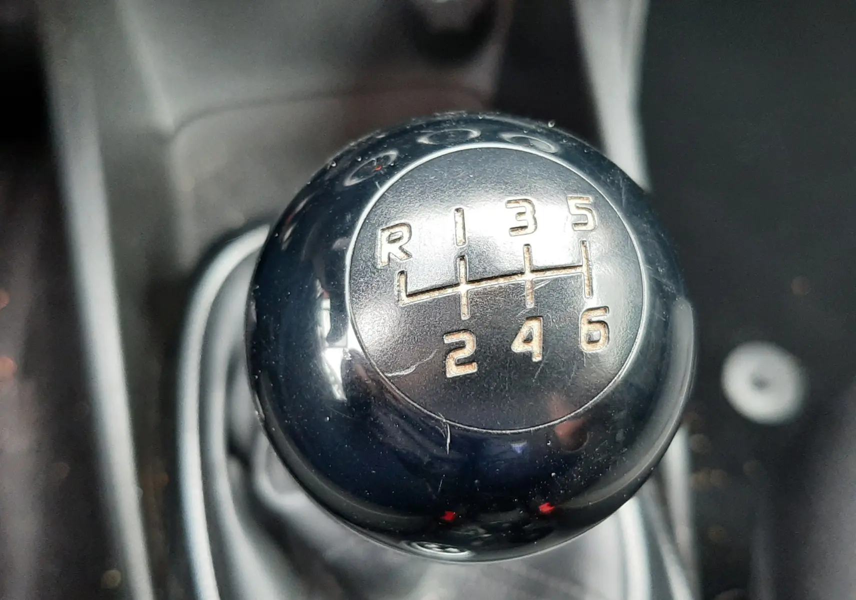 Gros plan sur le pommeau de la boîte manuelle 6 vitesses d'une Fiat 500X rouge, montrant les chiffres et la marche arrière.