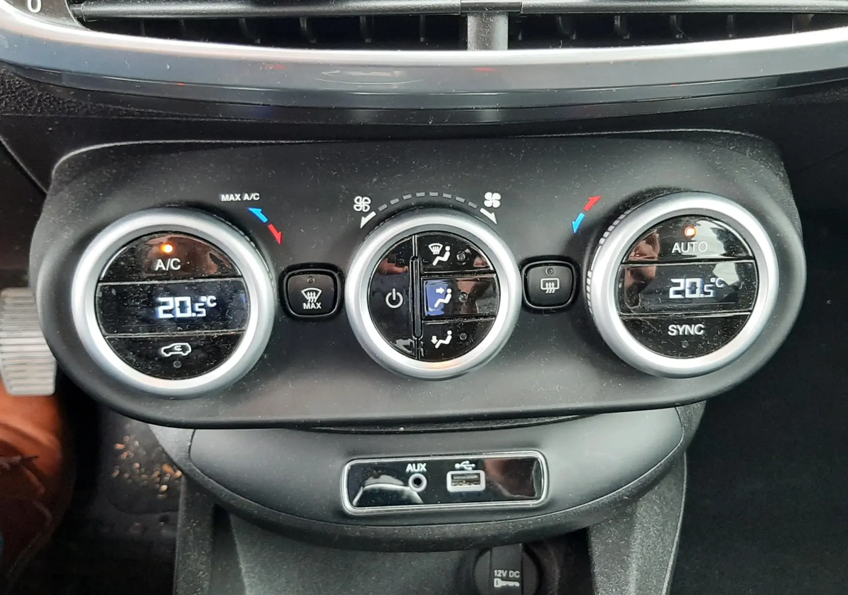 Gros plan sur les commandes de climatisation automatique et les prises AUX et USB du tableau de bord d'une Fiat 500X rouge.