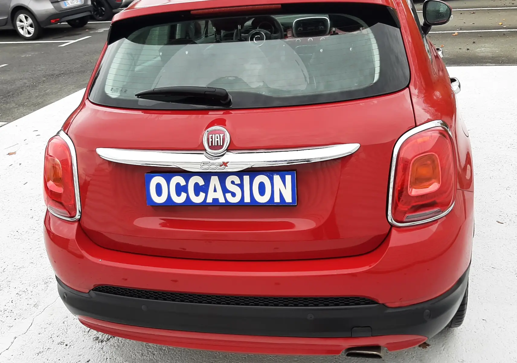 Vue arrière d'une FIAT 500X rouge avec plaque "OCCASION" sur un parking extérieur.