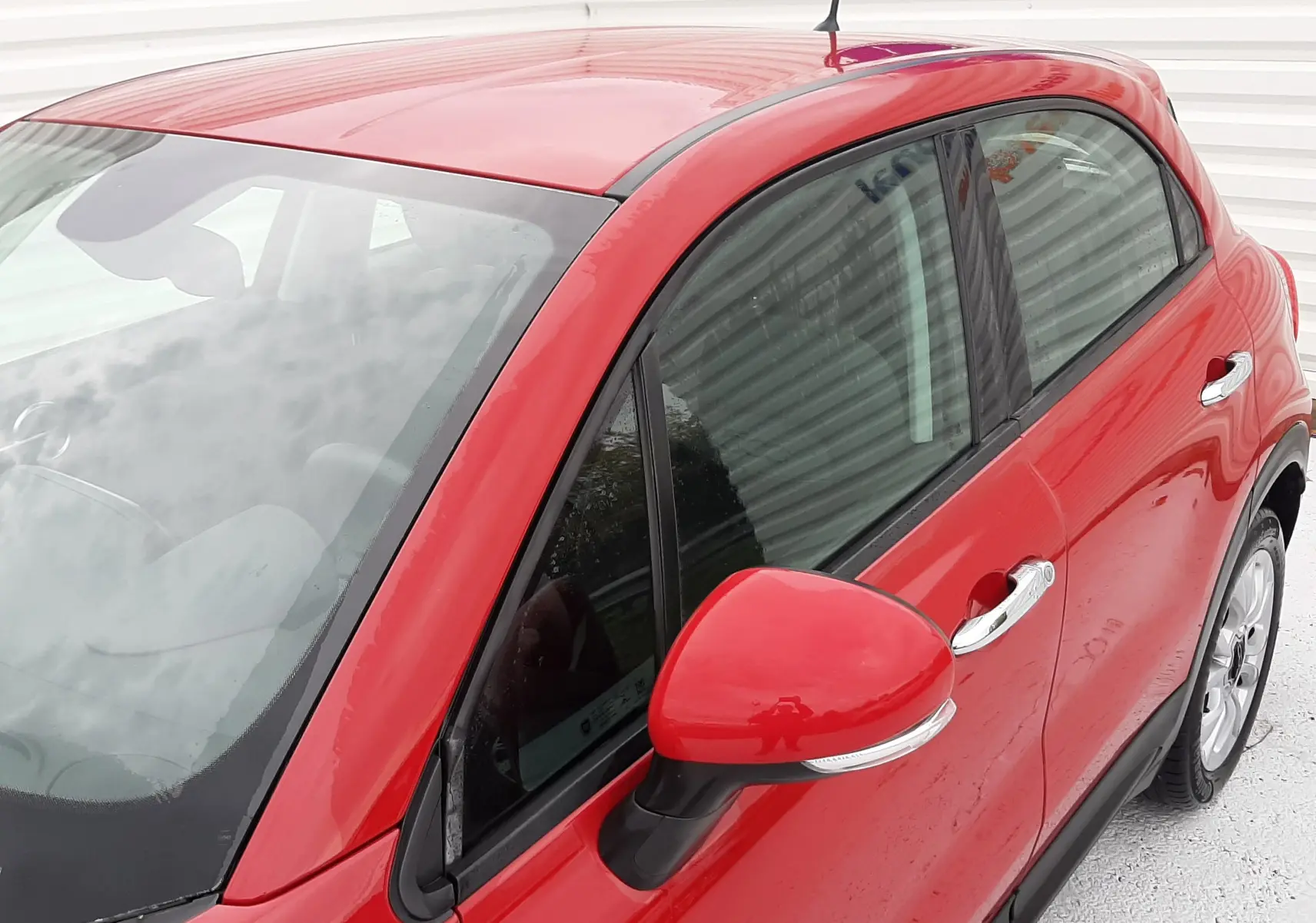 Vue 3/4 avant droit d'une FIAT 500X rouge avec rétroviseur et poignées chromées sur fond clair.