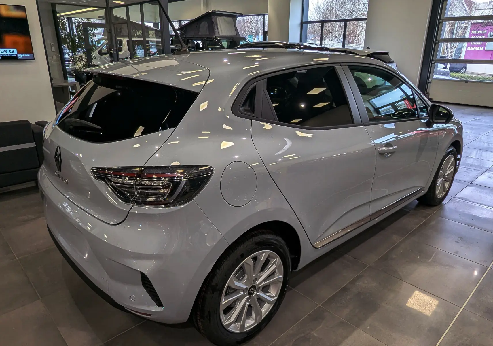 Vue 3/4 arrière droite d'une Renault Clio V Gris Rafale en showroom, avec vitres teintées et jantes alliage.