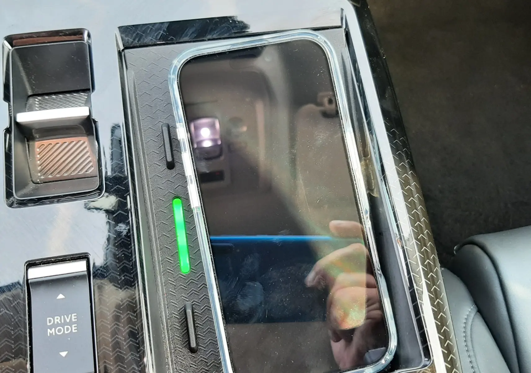 Gros plan sur la console centrale noire brillante du Citroën C5 Aircross hybride avec un smartphone en charge sans fil.