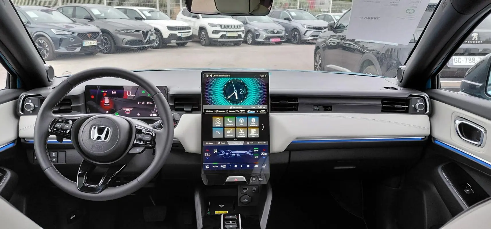 Vue intérieure avant du tableau de bord du Honda e:Ny1 bleu 2025 avec écran tactile vertical et éclairage d'ambiance bleu.