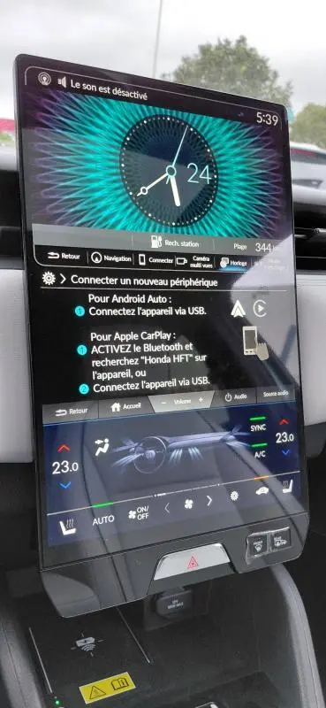 Vue rapprochée de l’écran tactile central du Honda e:Ny1 204 ch Advance 2025, affichant l’horloge et les réglages climatiques.
