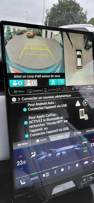 Écran intérieur de la Honda e:Ny1 204 ch Advance bleu montrant la caméra de recul et vue 360° en stationnement.