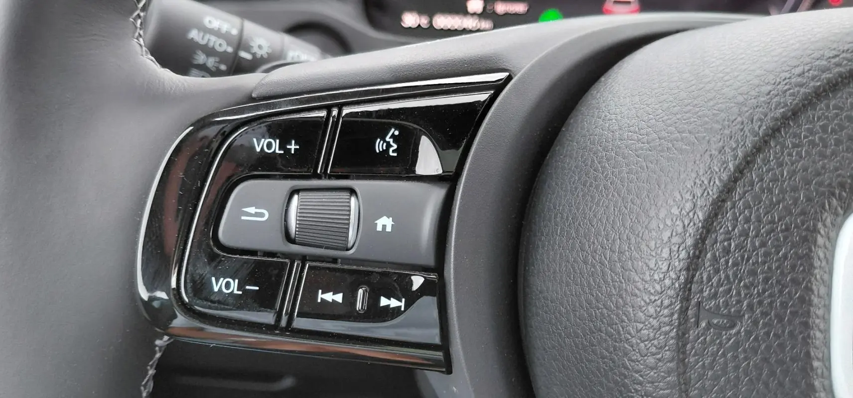 Gros plan sur les commandes de volume et multimédia au volant du Honda e:Ny1 204 ch Advance 2025, intérieur noir.