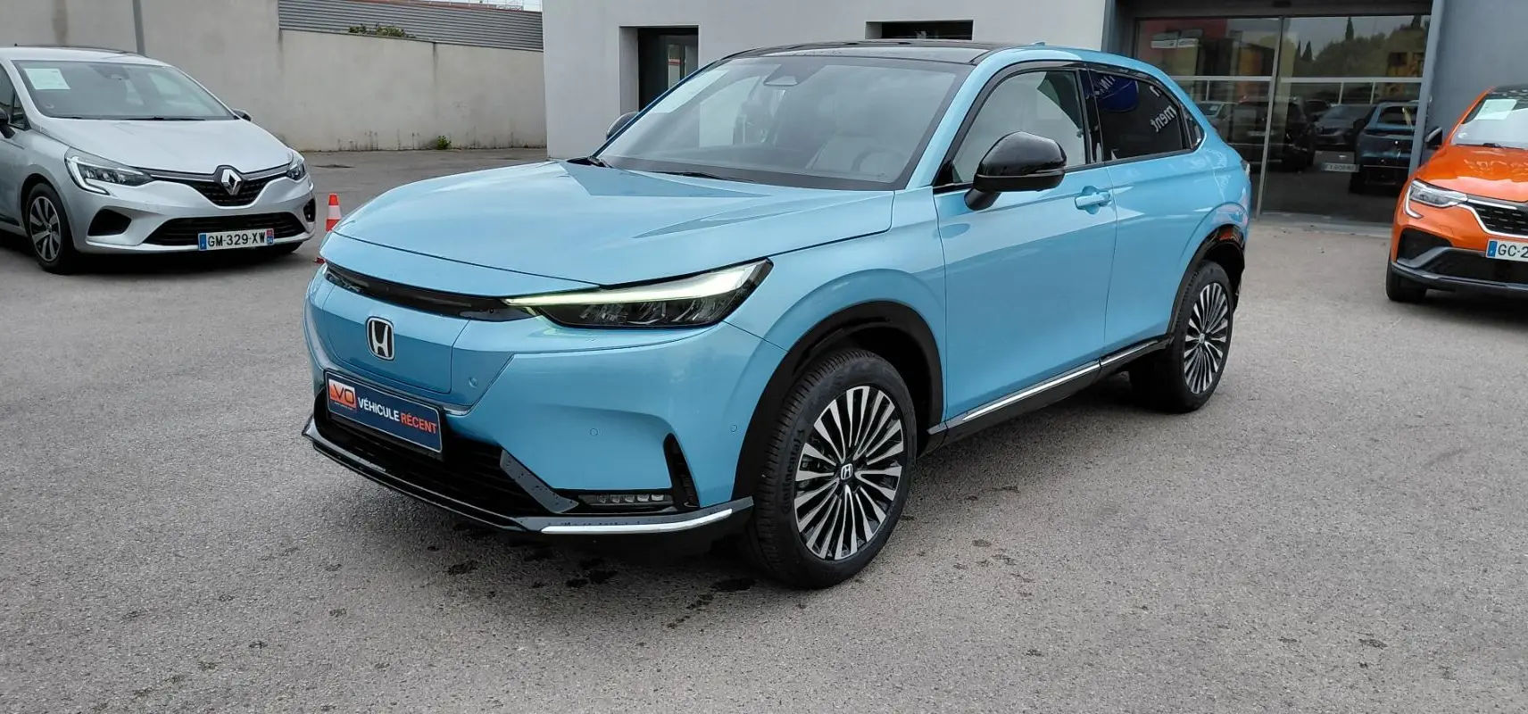 Vue 3/4 avant droite du Honda e:Ny1 Advance 204 ch bleu électrique avec jantes stylisées et toit noir.