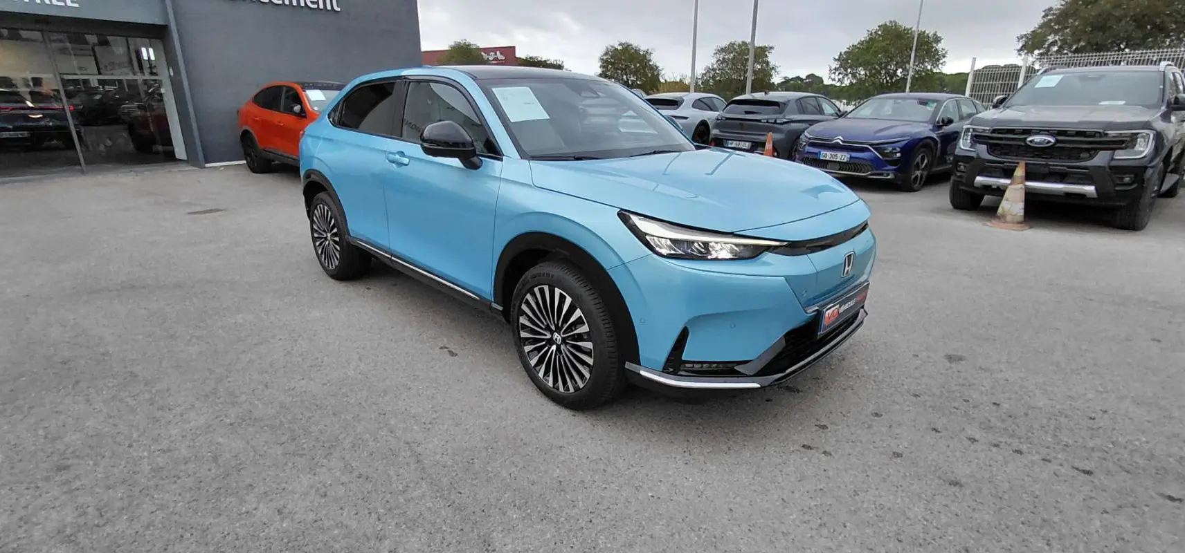Honda e:Ny1 204 ch Advance bleu électrique vu en 3/4 avant droit, avec calandre épurée et jantes stylées.