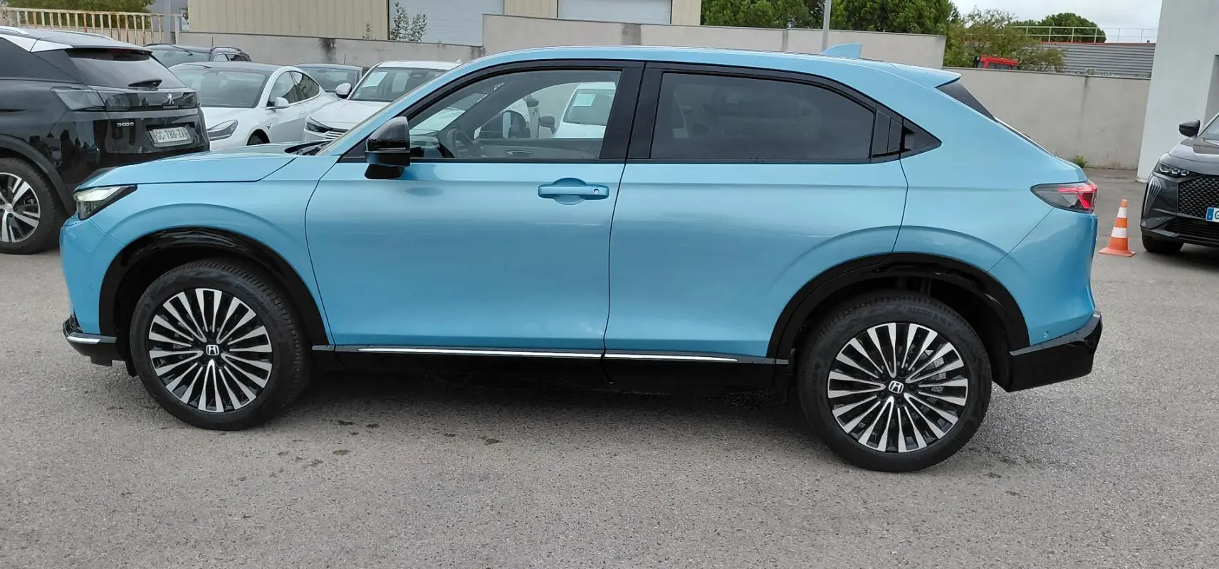 Vue de profil côté gauche d'un Honda e:Ny1 Advance 204 ch bleu électrique avec jantes stylisées en concession.