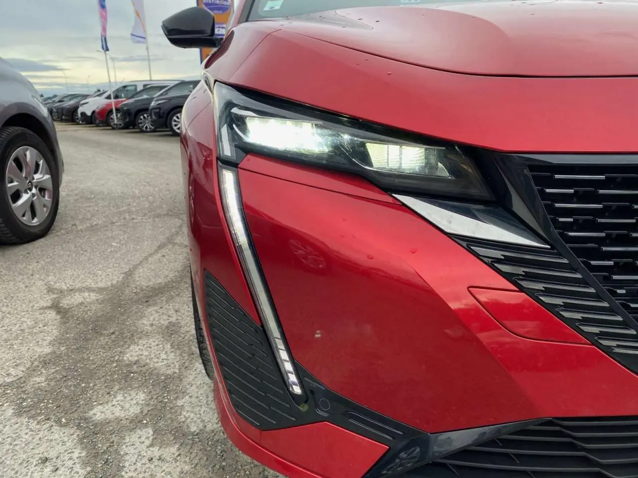 Gros plan sur l'avant droit de la Peugeot 308 rouge Elixir avec ses phares LED et la calandre noire distinctive.