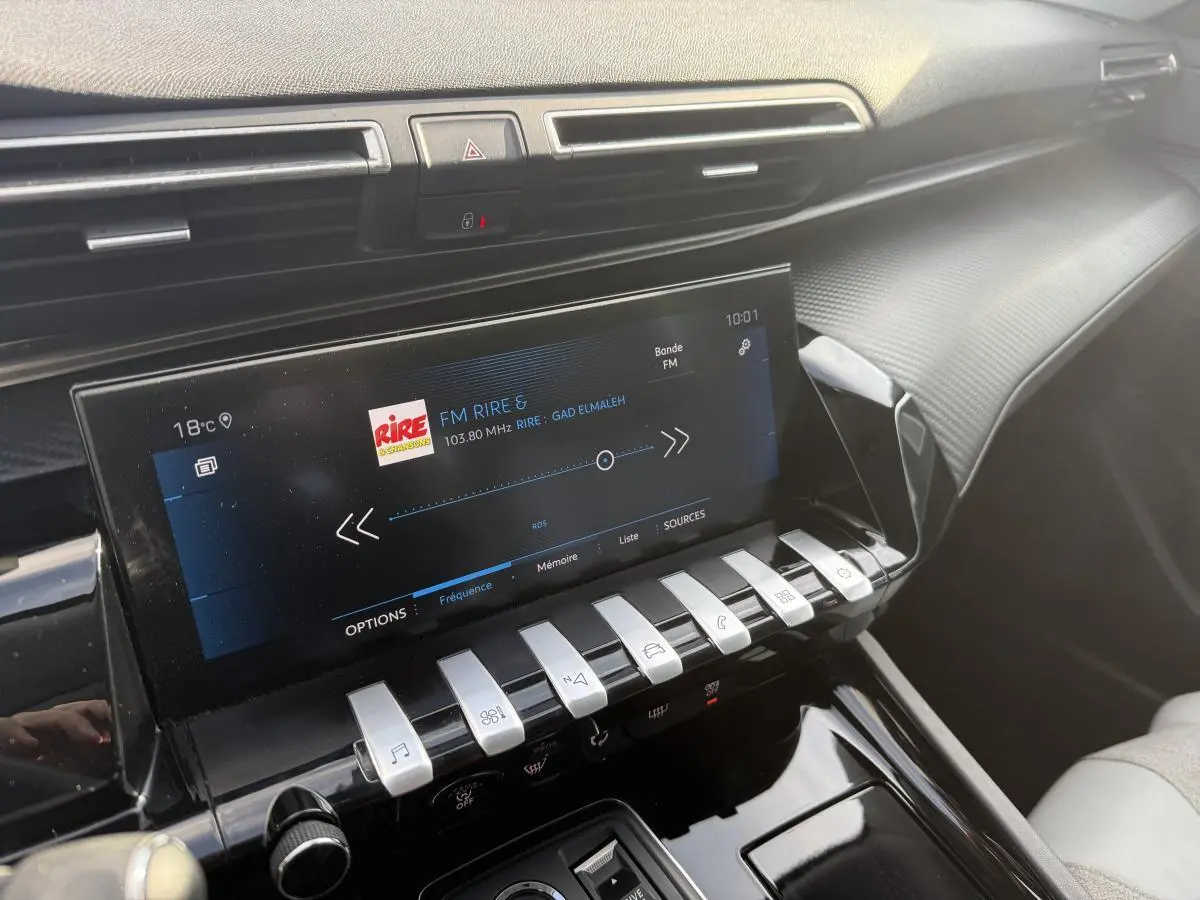 Vue rapprochée de la console centrale intérieure de la Peugeot 508 bleue, avec écran tactile et commandes piano chromées.