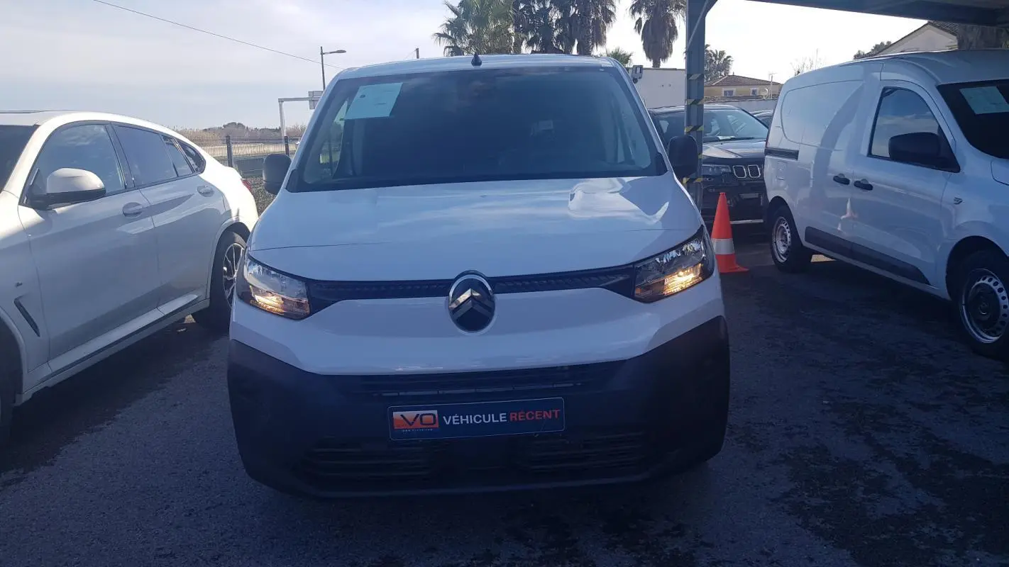 Vue avant d’un Citroën Berlingo blanc 2025 avec feux allumés, garé parmi d’autres véhicules en extérieur.