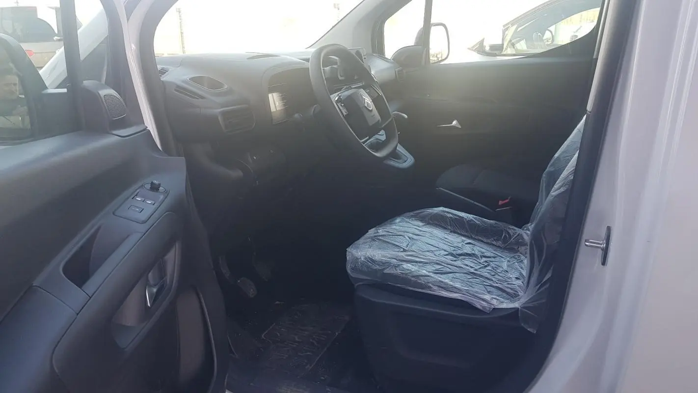 Vue intérieure côté conducteur du Citroën Berlingo blanc 2025, siège protégé par housse plastique et volant multifonctions.