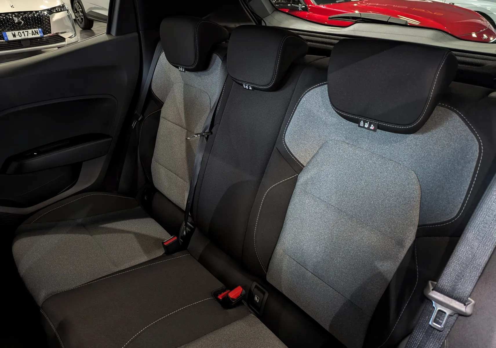 Vue intérieure sur les sièges arrière en tissu gris et noir de la Renault Clio V 2025, avec ceintures de sécurité visibles.