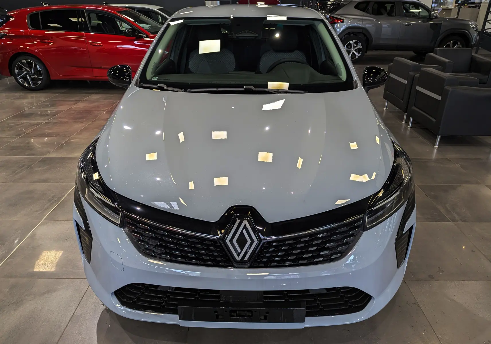 Vue avant rapprochée d’une Renault Clio V gris Rafale en showroom, mettant en valeur sa calandre noire et ses phares fins.