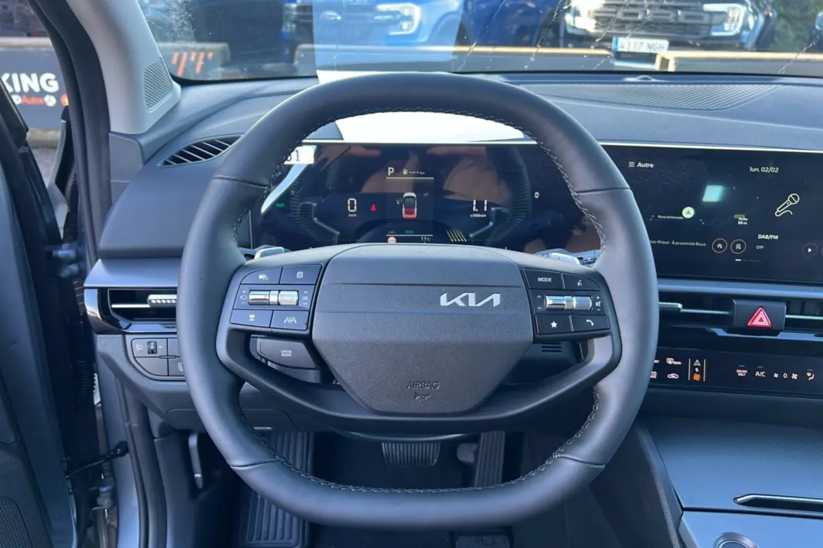 Vue intérieure centrée sur le volant cuir multifonctions du Kia Sportage 1.6 T-GDI HEV gris perle avec tableau de bord digital.