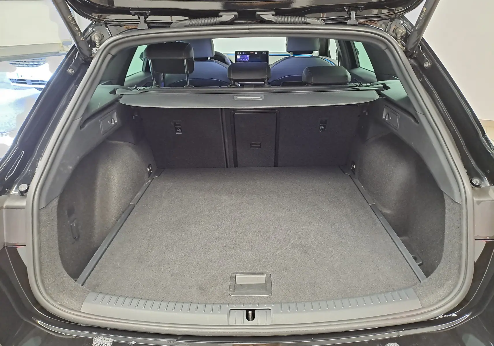 Coffre ouvert vu de l'arrière d'une CUPRA LEON ST 1.5 eTSI 150 DSG7 Noir Minuit, intérieur spacieux et tapis gris.
