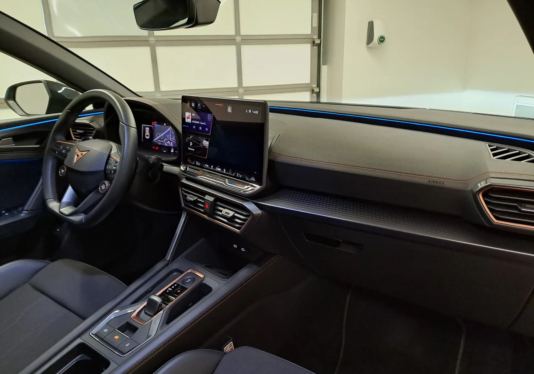 Vue intérieure côté conducteur de la CUPRA LEON ST 1.5 eTSI 2025, tableau de bord noir avec éclairage bleu et console centrale moderne.