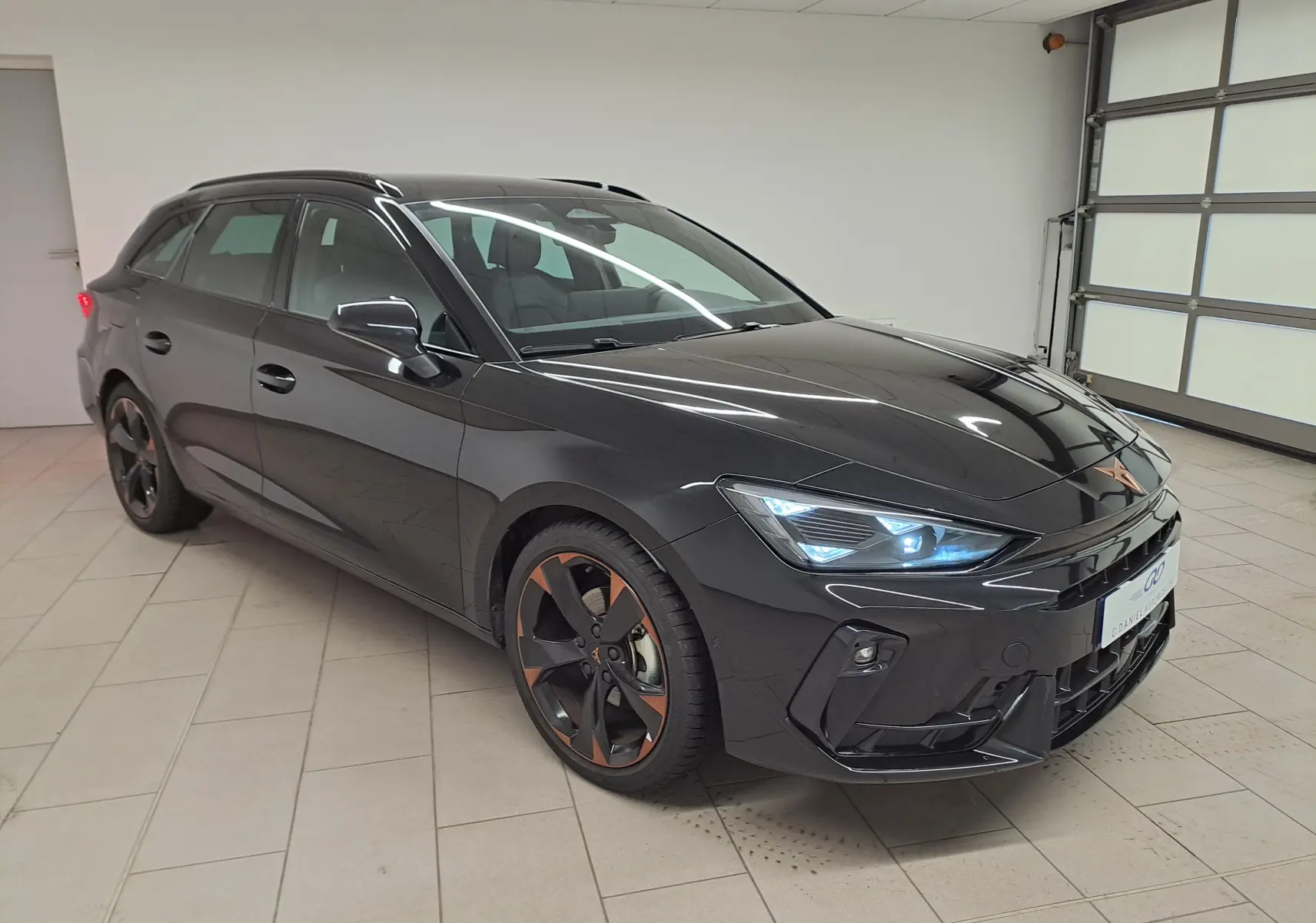 Vue 3/4 avant droite d'une CUPRA Leon ST 1.5 eTSI 150 DSG7 noire Minuit avec jantes alliage 18'' cuivrées en intérieur.