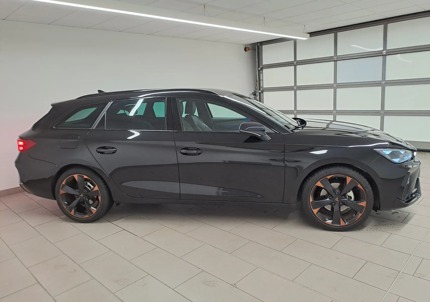 Vue de profil côté gauche d'une CUPRA LEON ST 2025 noire minuit avec jantes alliage 18'' cuivrées en intérieur lumineux.