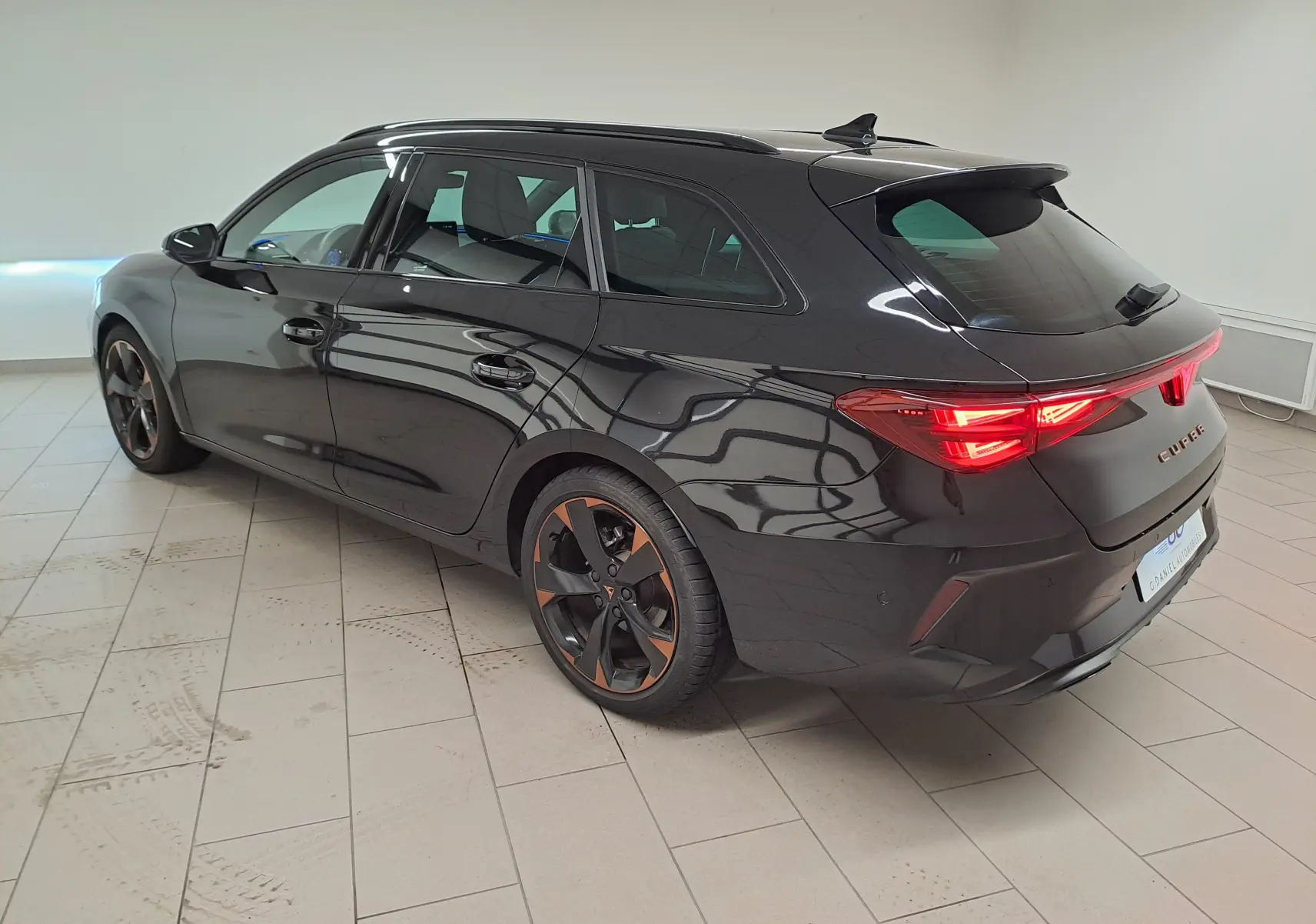 Vue 3/4 arrière droite de la CUPRA Leon ST 1.5 eTSI noire Minuit avec jantes alliage 18'' cuivrées et feux arrière allumés.