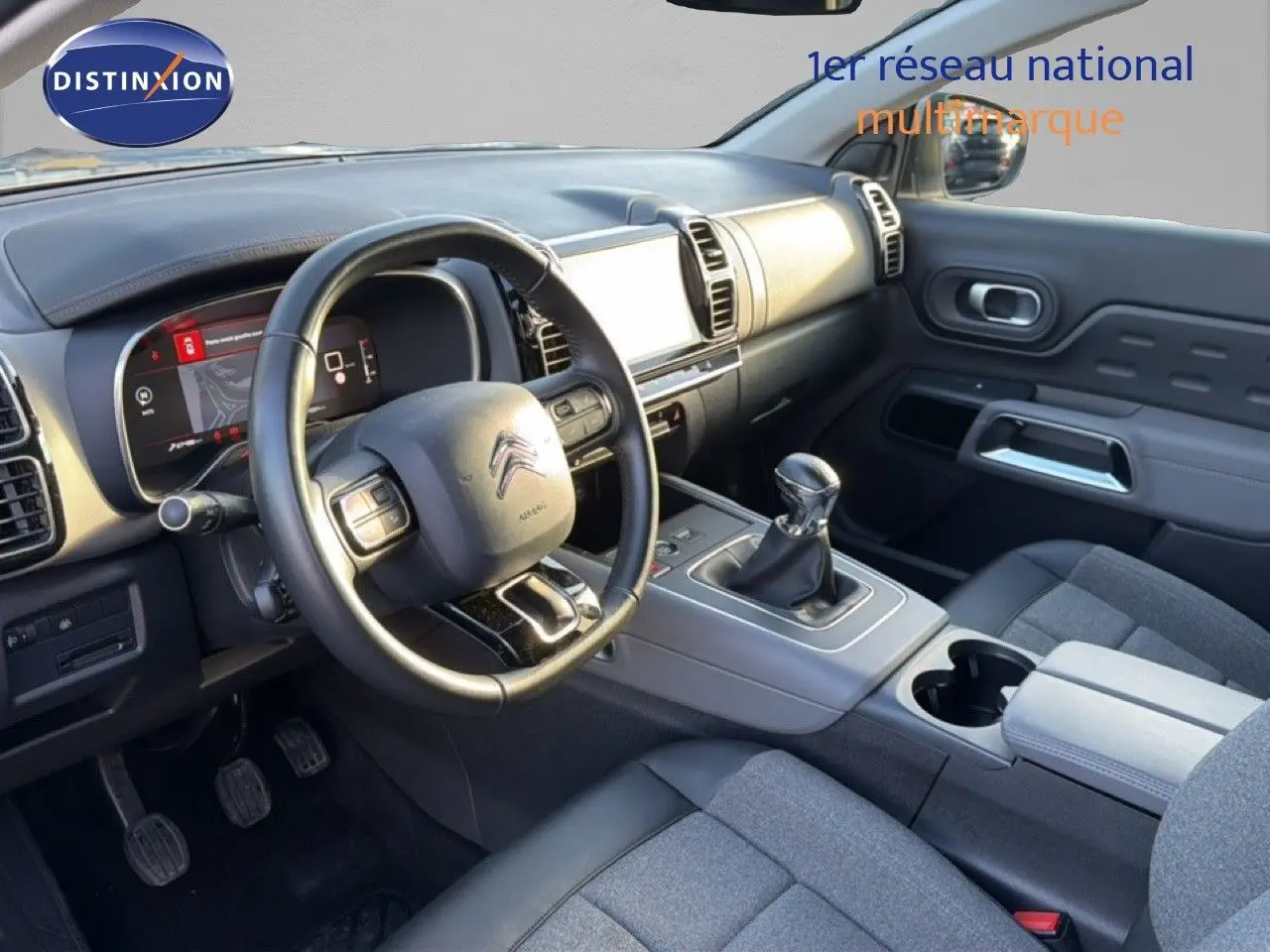 Vue intérieure côté conducteur du Citroën C5 Aircross gris, montrant le volant, tableau de bord numérique et levier de vitesse manuel.