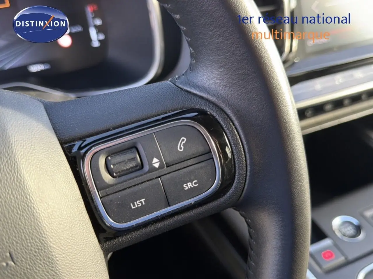 Gros plan sur les commandes gauche du volant en cuir noir du Citroën C5 Aircross gris Artense, tableau de bord en arrière-plan.